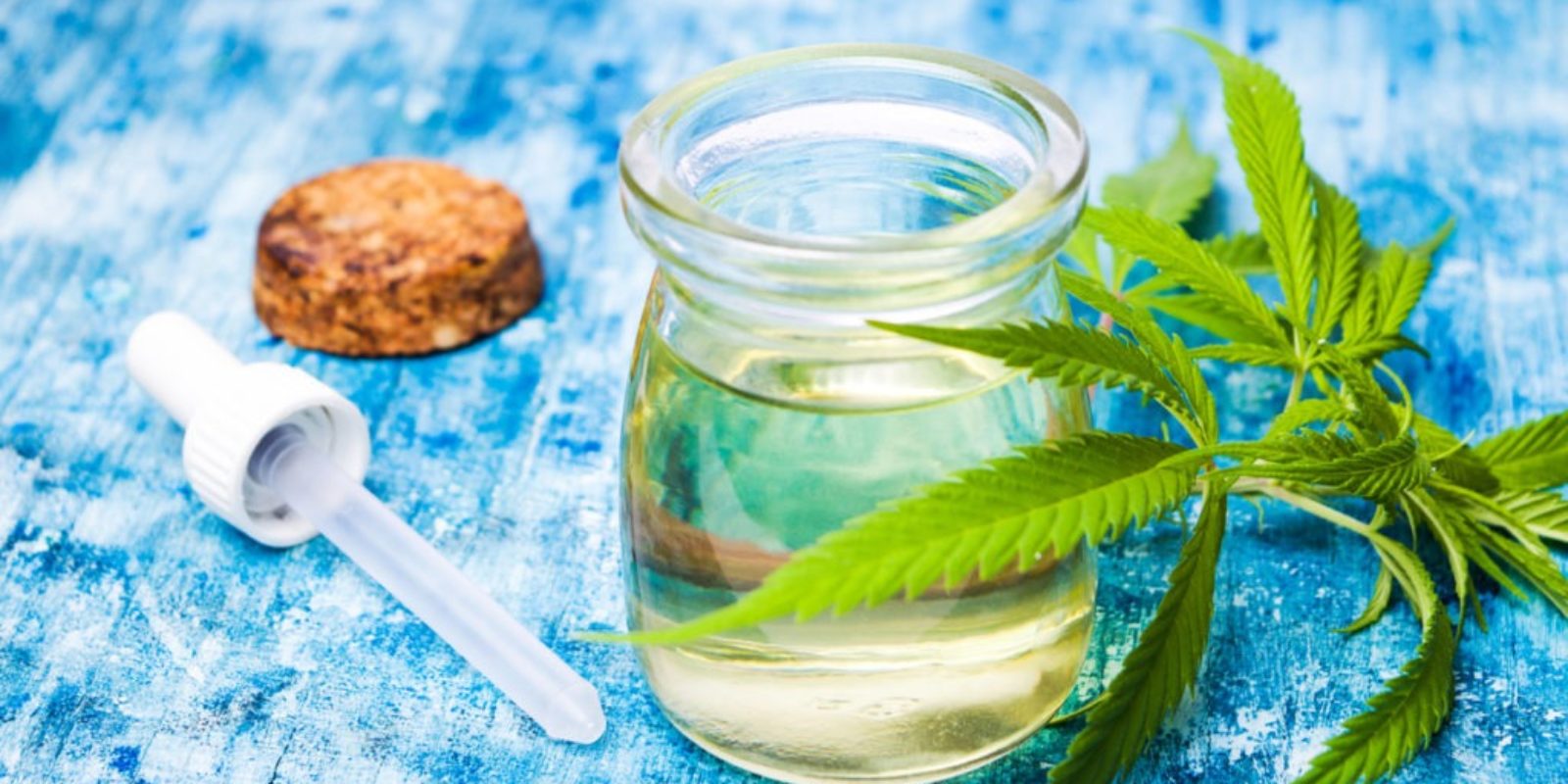 glass-container-of-hemp-cbd-oil-on-table-with-dropper-and-cannabis-leaves