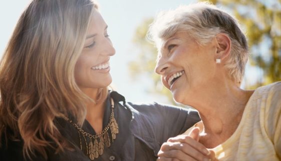 mother and adult daughter smiling at each other outside
