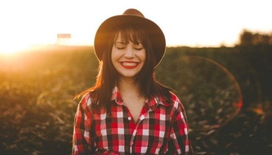 young-woman-wearing-brimmed-sunhat-and-red-checkered-shirt-smiling-in-field-during-golden-hour