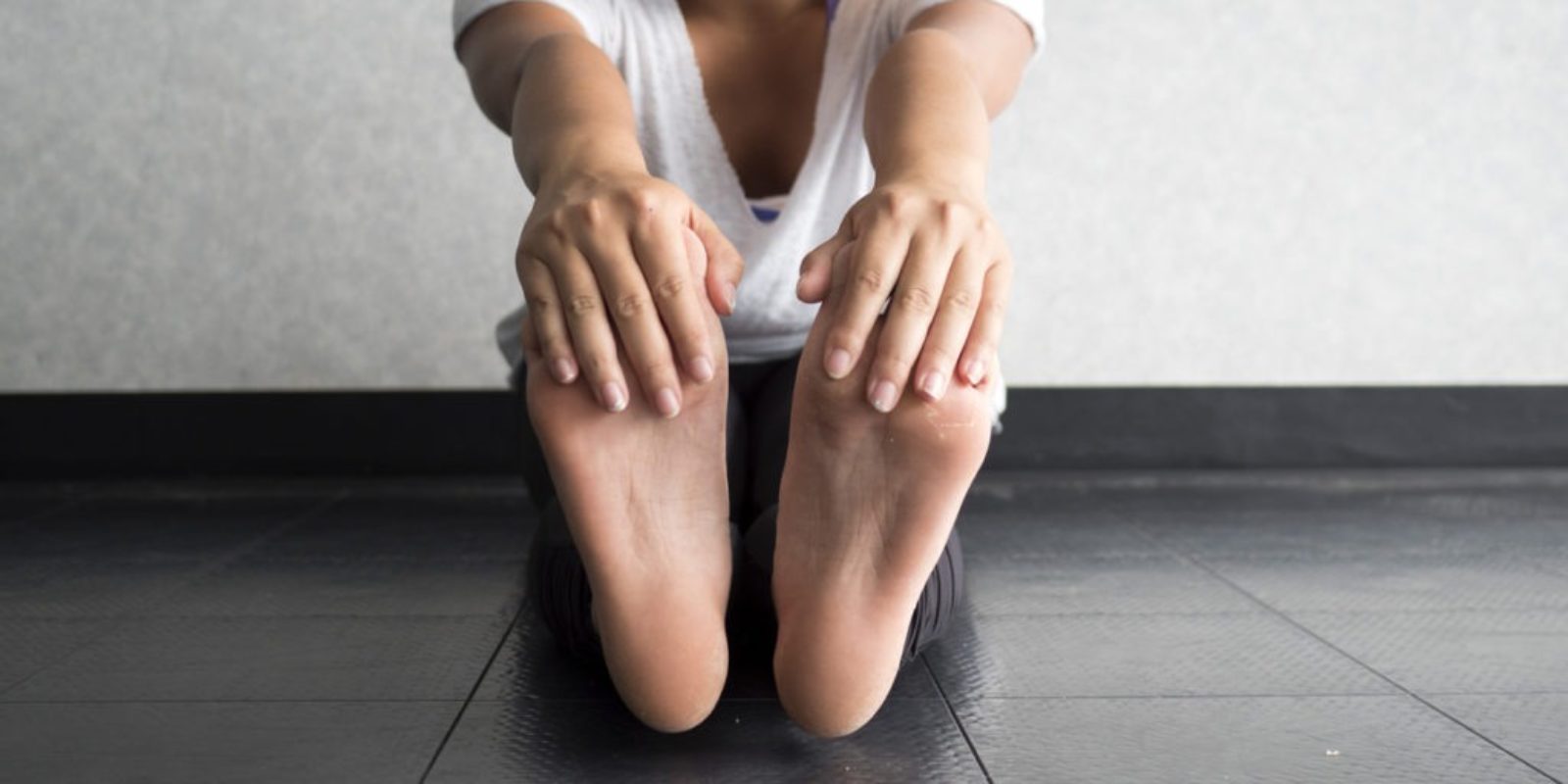 young woman sitting of floor with legs extended while holding toes to stretch hamstrings