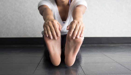 young woman sitting of floor with legs extended while holding toes to stretch hamstrings