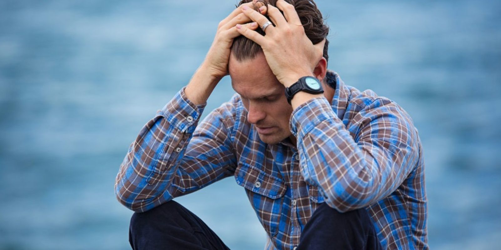 Man appears stressed out by holding his head and body crouched together.